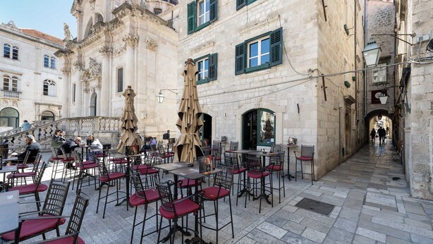 An outdoor café with tables and chairs, set against a historic building with ornate architecture and a dome.