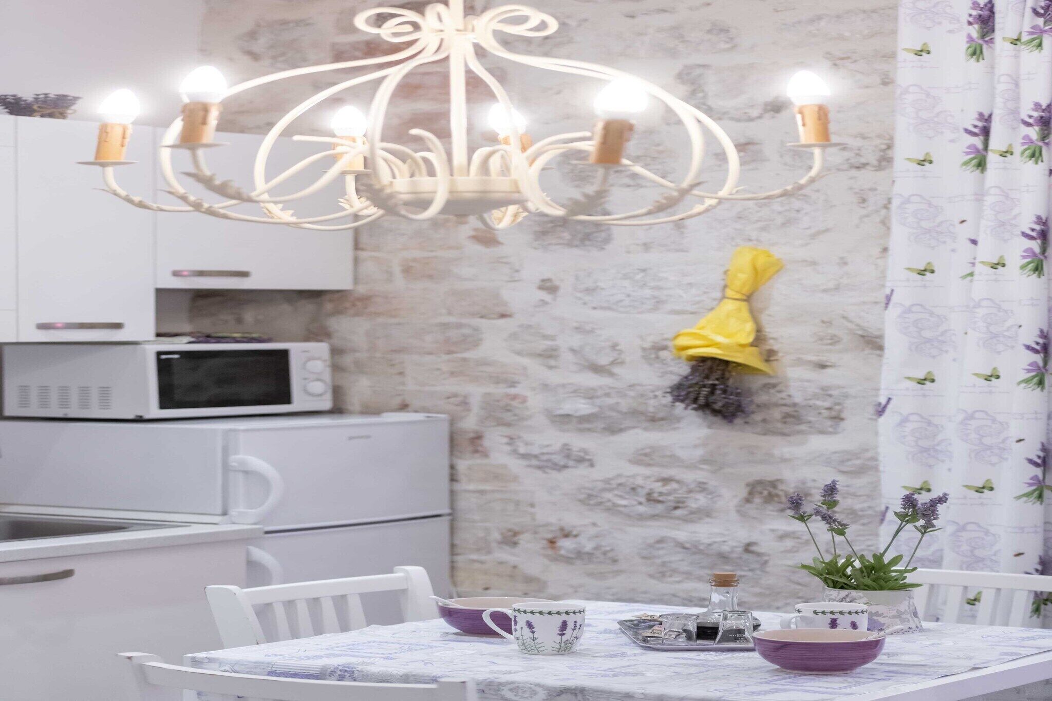 A dining area with a chandelier, white cabinets, a microwave, and a table with chairs.