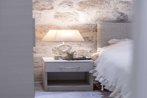 Ein Schlafzimmer mit Steinwand, Nachttisch mit Lampe und Bett mit weißer Bettdecke.