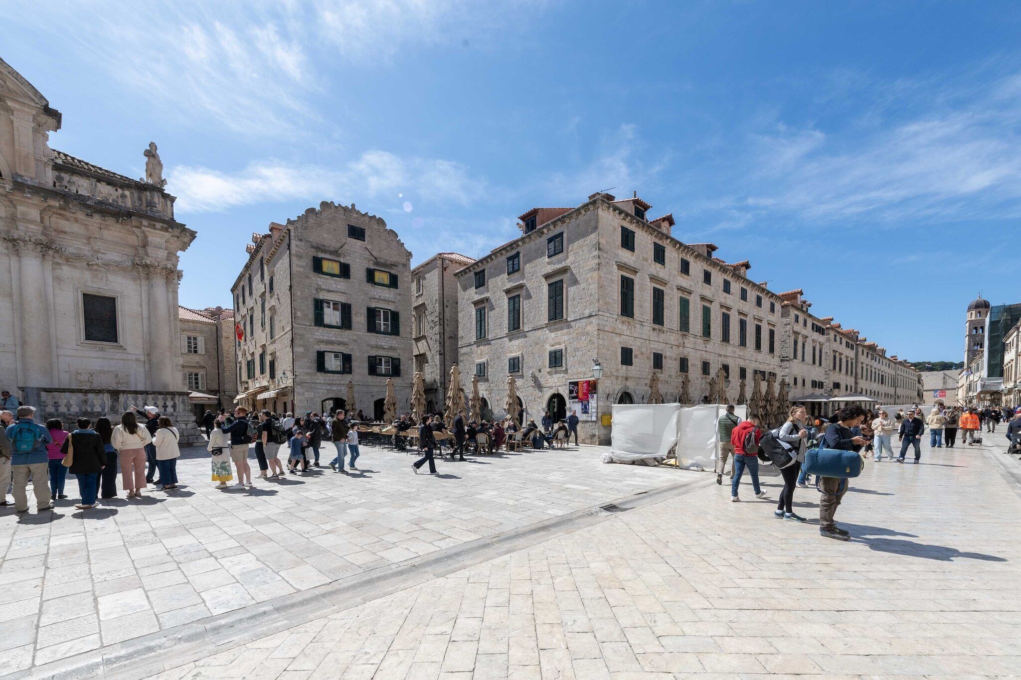 A historic square with stone buildings, outdoor seating, and a clear sky.