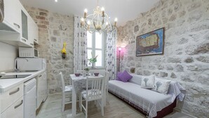 A room with a stone wall, a bed with striped bedding, a dining table with chairs, a chandelier, and a painting.