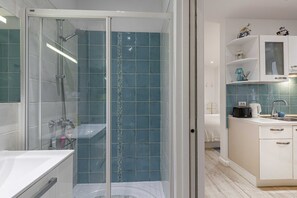 Un baño moderno con ducha de vidrio, lavamanos blanco y zona de ducha con azulejos azules.