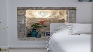 A bedroom with a stone wall, a small window, a bed with white bedding, and a decorative vase with flowers. - L & L Old Town Apartments - Studio Apartment ( Lacroma) (Dubrovnik)