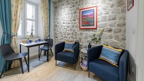 A room with a stone wall, a framed picture, two armchairs, a table with chairs, and a window with curtains. - L & L Old Town Apartments - Studio Apartment ( Lacroma) (Dubrovnik)