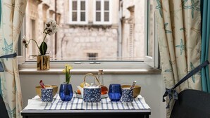 A table with blue and white patterned vases, a teapot, and a bottle, set against a window with starfish-patterned curtains. - L & L Old Town Apartments - Studio Apartment ( Lacroma) (Dubrovnik)