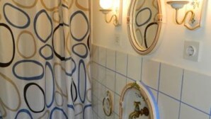 A bathroom with a patterned shower curtain, a wall-mounted mirror, and decorative tiles. - 2 bedroom apartment with terrace (Sumpetar)