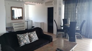 A living room with a black sofa, a coffee table, and a dining area with a table and chairs. There is a mirror on the wall, a small cabinet, and a door leading to another room. - Villa Elit- Three Bedroom Apartment with Sea View Terrace (Penthouse) (Sumpetar)