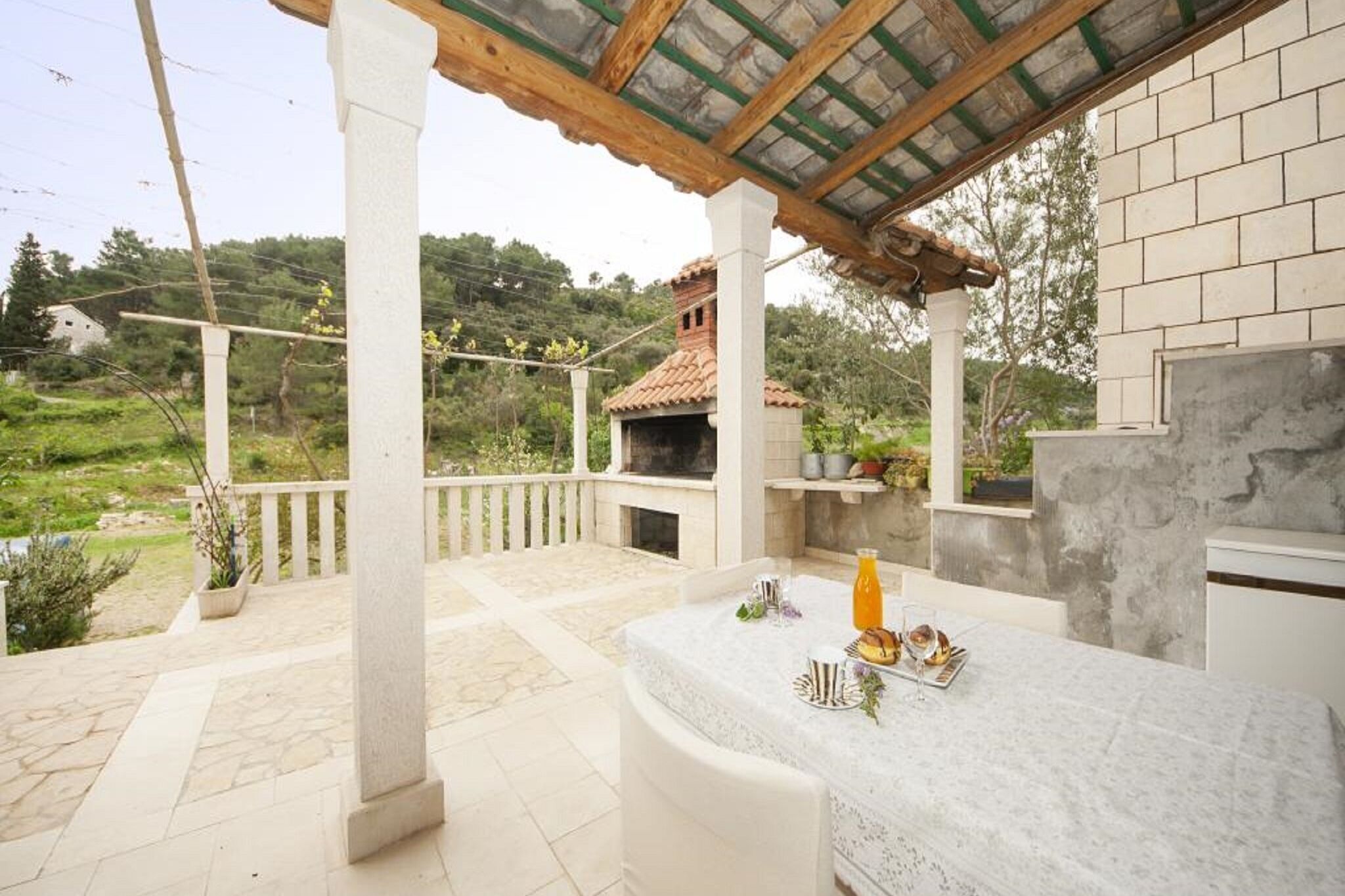 Un área de comedor al aire libre con una mesa dispuesta para dos, una parrilla y vistas a un jardín exuberante y colinas.
