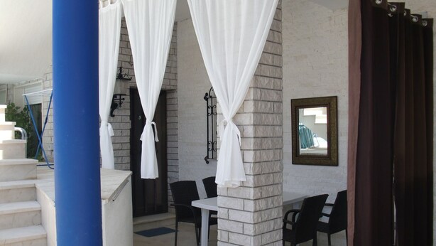 A covered outdoor seating area with white curtains, a stone wall, and a blue pillar. - Villa Elit - Comfort Two Bedroom Apartment with Terrace ( A5) (Sumpetar)