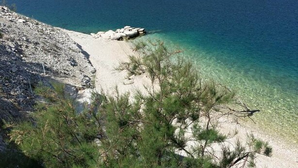 Une plage bordée d’une eau turquoise et limpide, avec un terrain rocheux et une végétation clairsemée.