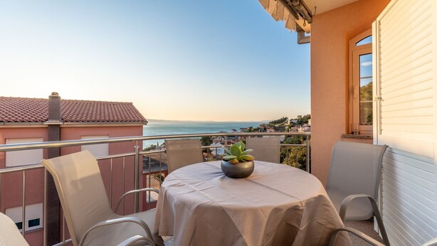 Een balkon met een tafel en stoelen, met uitzicht op de kust.