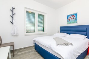 Quarto com cama, janela com persianas, um quadro na parede e uma cadeira.