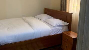 A single bed with white bedding, a wooden headboard, a nightstand, and a striped rug on a wooden floor.