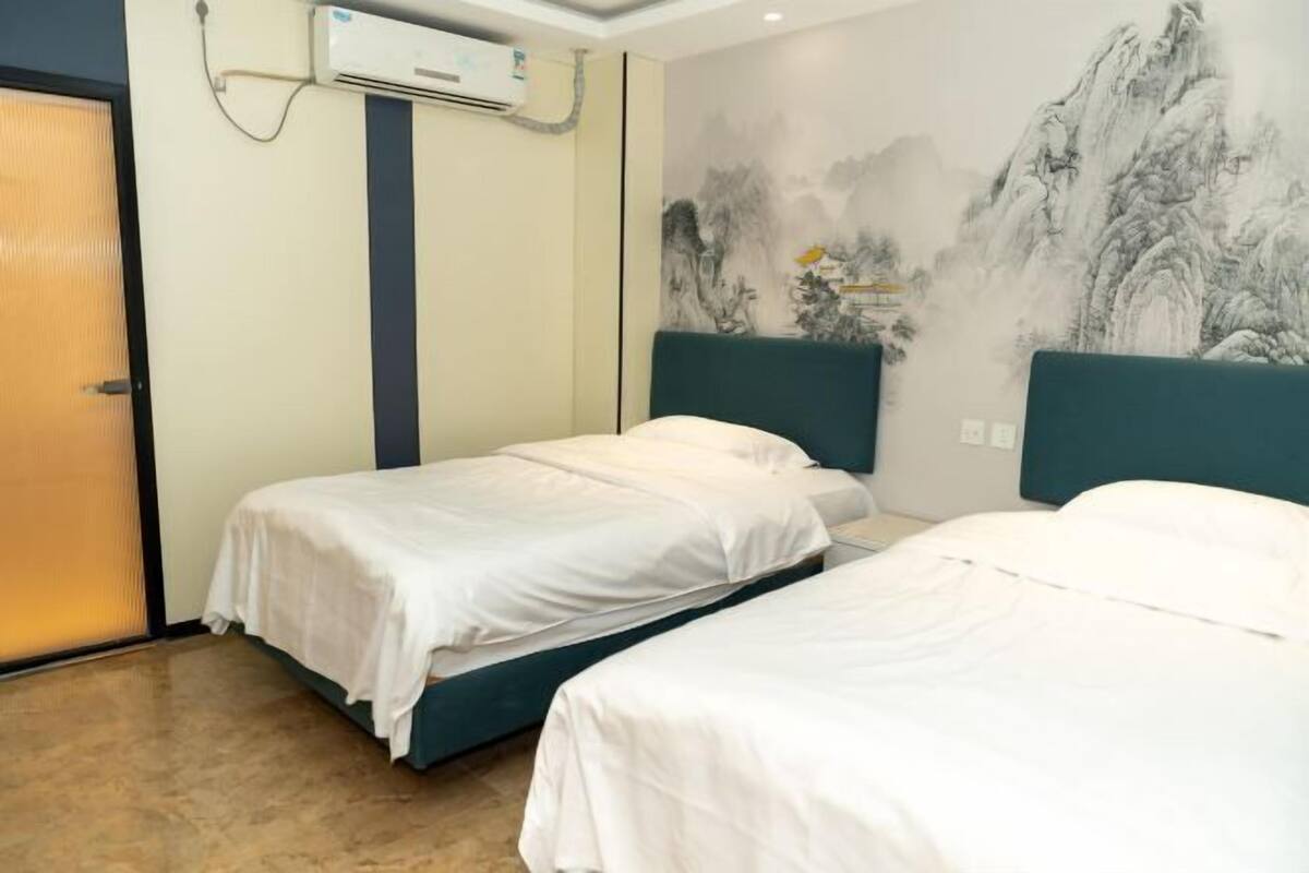 Habitación de hotel con dos camas, aire acondicionado en la pared y un cuadro grande de un paisaje montañoso.
