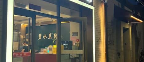 L’entrée d’un hôtel, avec une porte en verre, un comptoir d’accueil et une enseigne portant des caractères chinois.