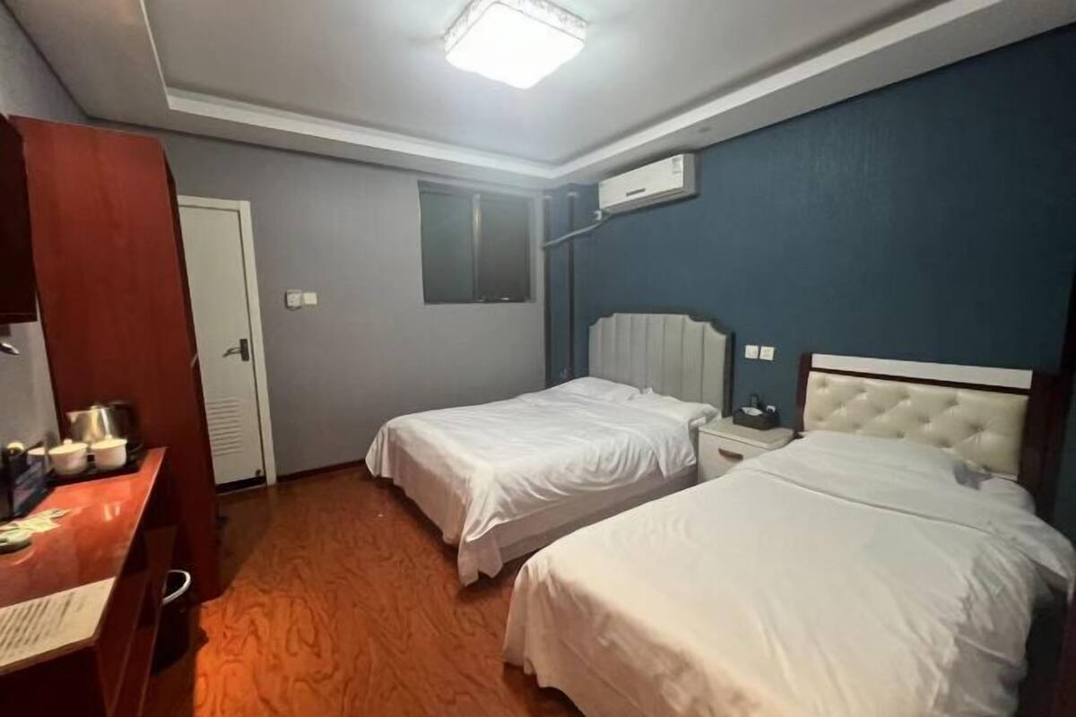 Habitación de hotel con dos camas, un escritorio con silla, armario, espejo y aire acondicionado.