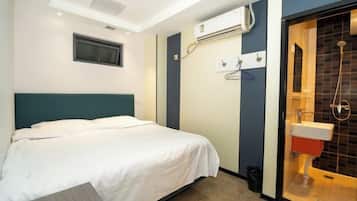 A hotel room with a bed, an air conditioning unit, a shower area, and a window.