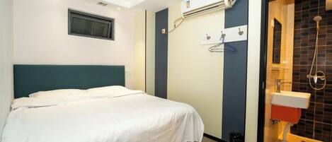 A hotel room with a bed, an air conditioning unit, a shower area, and a window.
