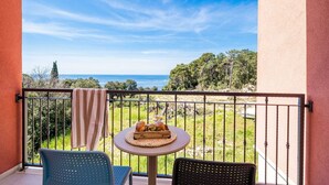 A balcony with a table set for two, overlooking a grassy area and the sea.