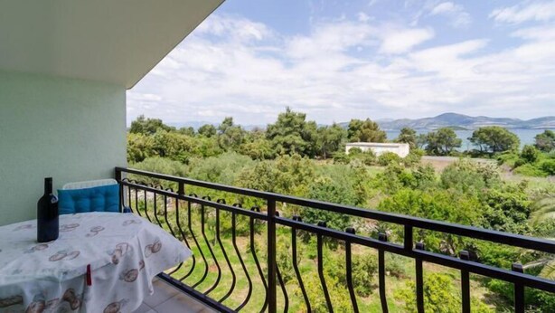A balcony with a table and chairs, overlooking a lush landscape with trees and a body of water.