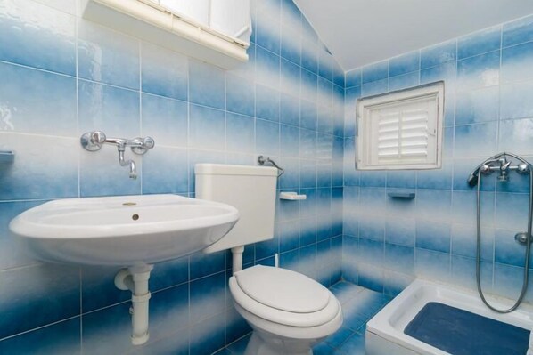 Un baño con lavamanos, inodoro y bañera blancos, todo sobre un fondo de paredes con azulejos azules.