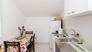 A compact kitchen with a dining table, chairs, a refrigerator, a sink, and a stove.