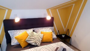 A bedroom with a bed, pillows, a bedside table, and a wall with geometric patterns. - Apartments Villa Bell Memories-Studio Apartment with Balcony and Sea View (A2) (Cavtat)