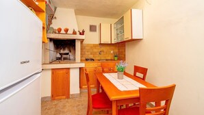 Een kleine keuken met een ingebouwde grill, houten kastjes, een eettafel met stoelen en een koelkast.