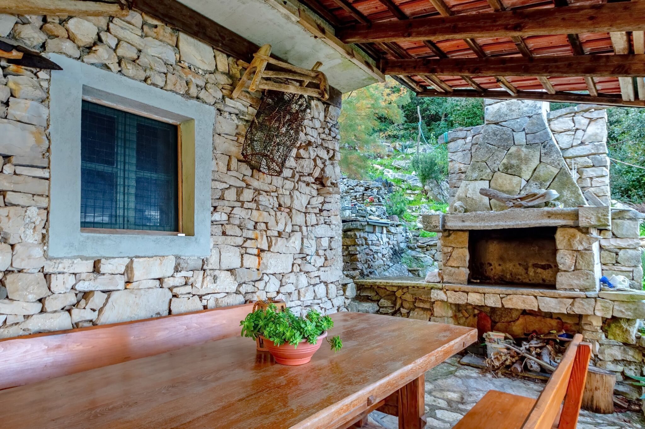 Un espacio al aire libre con paredes de piedra, una mesa y bancos de madera, un horno de piedra y una ventana.
