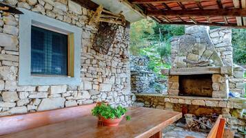 Un espacio al aire libre con paredes de piedra, una mesa y bancos de madera, un horno de piedra y una ventana.