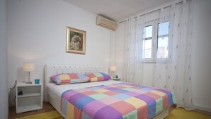 A bedroom with a bed, two bedside tables, a nightstand, a wall-mounted air conditioner, a window with curtains, and a framed picture on the wall. - Holiday home  Ingrid - Four Bedroom Holiday Home with Pool (Okrug Gornji)