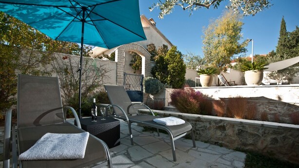 An outdoor seating area with two lounge chairs and a large blue umbrella, surrounded by stone walls and potted plants. - Holiday home  Ingrid - Four Bedroom Holiday Home with Pool (Okrug Gornji)