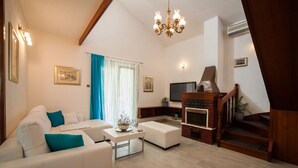 A living room with a white sofa, a TV, a fireplace, and a staircase. - Holiday home  Ingrid - Four Bedroom Holiday Home with Pool (Okrug Gornji)