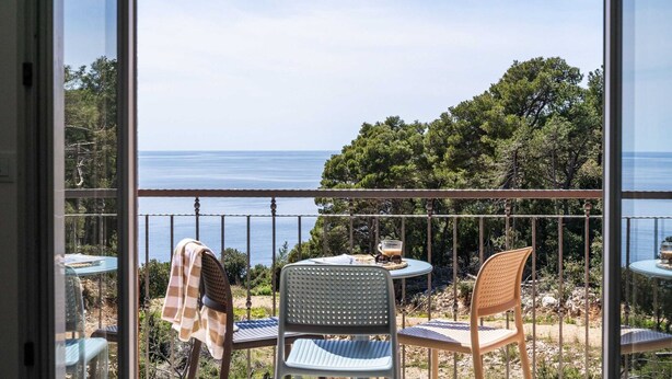 Een balkon met een tafel en stoelen, met uitzicht op een prachtig zee- en boslandschap.