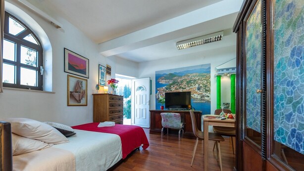 Habitación de hotel con cama, escritorio, silla, televisor y cuadro de un paisaje costero.