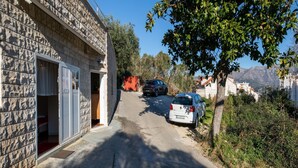 Una calle estrecha con coches aparcados, edificios de piedra y montañas a lo lejos.