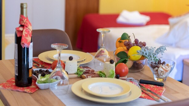 A dining table set with plates, cutlery, a bottle of wine, and various food items.