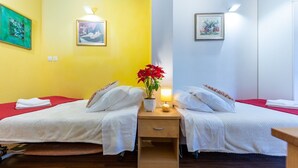 A hotel room with two beds, a wooden nightstand with a lamp, and artwork on the walls.