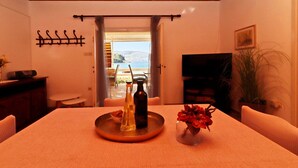 A dining area with a table set for two, a bottle of olive oil, a glass of water, and a vase with red flowers. There is a view of the sea through an open door. - Holiday Home Neda-Three Bedroom Holiday Home with Terrace and Sea View (Vela Luka)