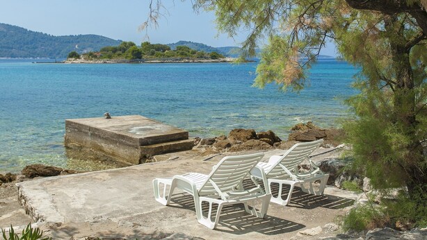 A beach with two white lounge chairs and a concrete platform by the water. - Holiday Home Neda-Three Bedroom Holiday Home with Terrace and Sea View (Vela Luka)
