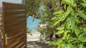 A wooden gate leading to a beach with clear blue water, surrounded by greenery and a stone pathway. - Holiday Home Neda-Three Bedroom Holiday Home with Terrace and Sea View (Vela Luka)