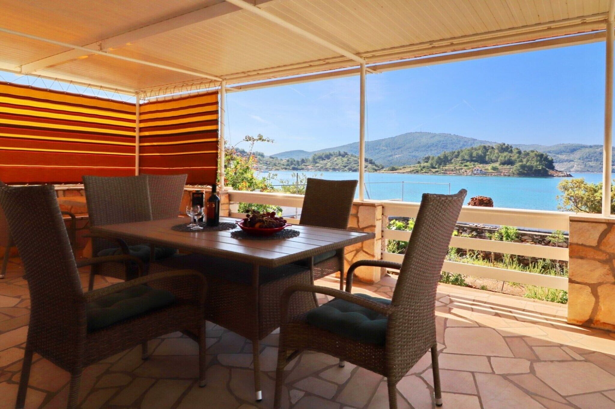 Uma área de refeições coberta ao ar livre, com cadeiras de vime e uma mesa, com vista para um lago e colinas panorâmicos.