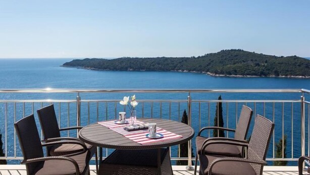 A round table with chairs on a balcony overlooking a body of water and a distant island.
