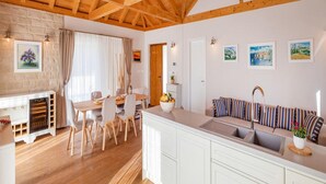 Et moderne køkken med træloft, hvide skabe, et spiseområde med bord og stole, samt en sofa med stribede hynder.
