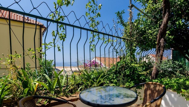 Ein Balkon mit rundem Tisch und Korbstühlen, der auf einen Garten und eine ferne Aussicht blickt.