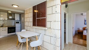 Eine moderne Küche mit weißen Schränken, einem eingebauten Backofen und einer Mikrowelle. Es gibt einen Essbereich mit einem weißen Tisch und Stühlen.