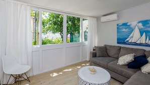 Ein Wohnzimmer mit einem großen Fenster, einem grauen Sofa, einem weißen Sessel und einem Gemälde mit Segelbooten.