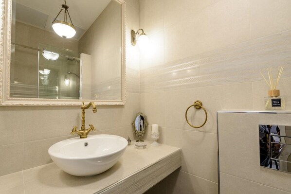 Een badkamer met een wit wastafel, een gouden kraan en een grote spiegel.