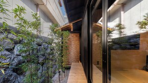 A modern interior with a wooden walkway, bamboo plants, and a glass door leading to a seating area. - Kanade GionRokuhara (Kyoto)