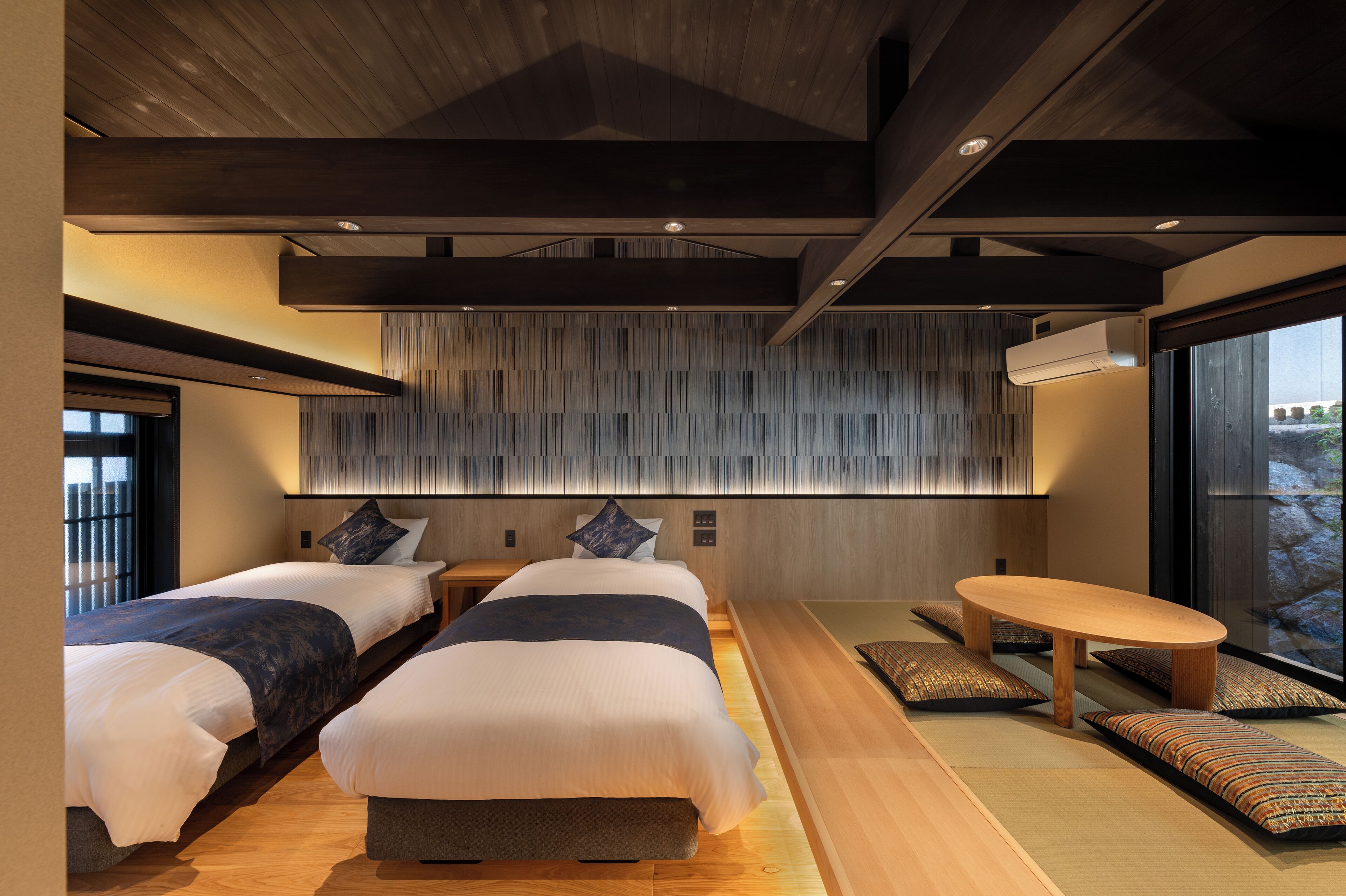A modern hotel room with two beds, a wooden ceiling, a large window, and a small round table.